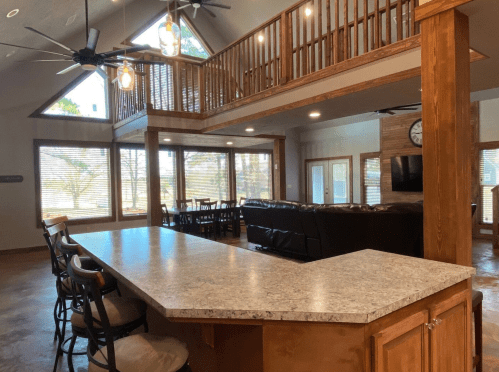 Spacious interior of a modern cabin with a kitchen bar, dining area, and large windows overlooking nature.
