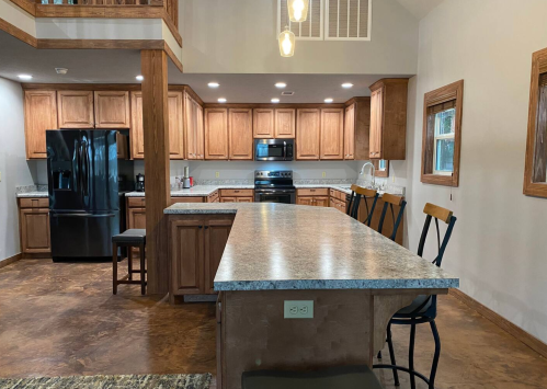 Modern kitchen with wooden cabinets, black appliances, and a large island with bar stools. Bright and spacious design.