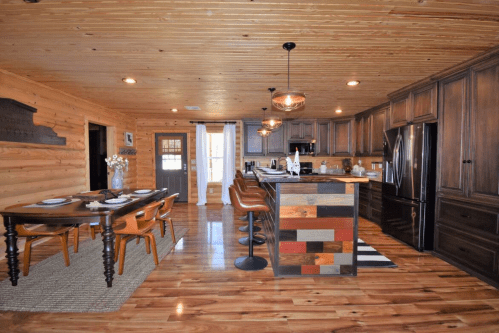 A cozy wooden kitchen with a dining table, bar stools, and modern appliances, featuring warm lighting and rustic decor.