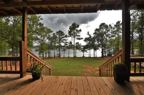 View from a wooden deck overlooking a lake surrounded by tall trees under a cloudy sky.