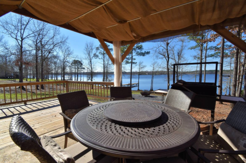 A lakeside patio with a round table and chairs, overlooking a serene lake surrounded by trees.