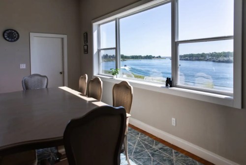A dining area with a table and chairs, featuring a large window overlooking a scenic water view.