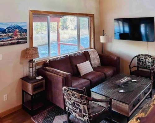Cozy living room with a brown sofa, wooden coffee table, TV, and scenic artwork by the window.