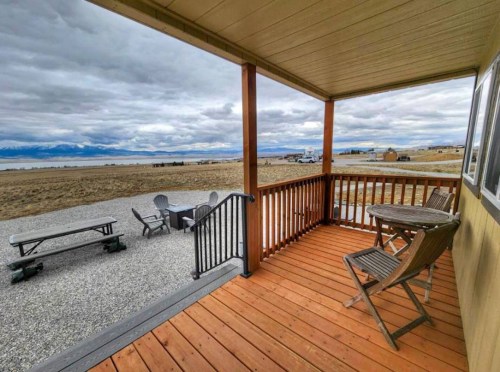 A wooden porch with a table and chairs overlooks a vast, open landscape under a cloudy sky.