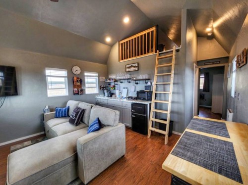 Cozy interior of a small living space featuring a sofa, kitchenette, and a loft accessed by a wooden ladder.