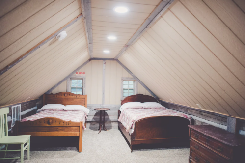 Cozy attic bedroom with two wooden beds, a small table, and a rustic decor under a sloped ceiling.