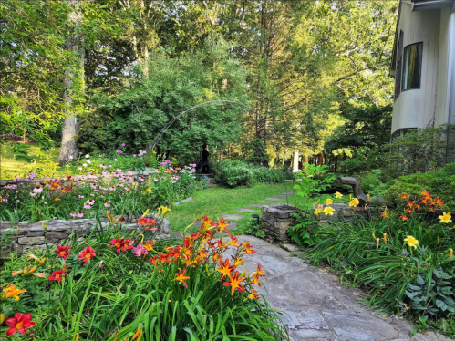 A vibrant garden path lined with colorful flowers, leading to a lush green area and a house in the background.