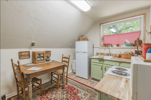 Cozy kitchen with a wooden table, chairs, green cabinets, and a window overlooking greenery.