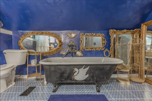 A vintage bathroom with a blue wall, a black clawfoot tub, ornate mirrors, and decorative accents.