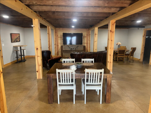 Cozy basement living area with a dining table, chairs, leather sofas, and a TV on a wooden cabinet.