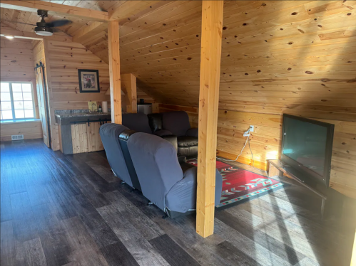 Cozy wooden loft with a seating area, small kitchenette, and a TV, featuring warm lighting and rustic decor.