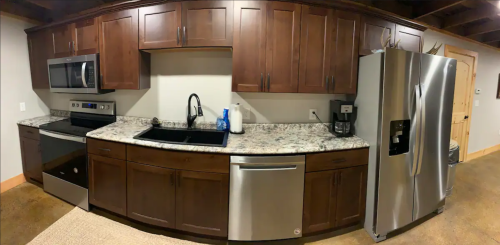 Modern kitchen with dark wood cabinets, stainless steel appliances, granite countertops, and a black sink.