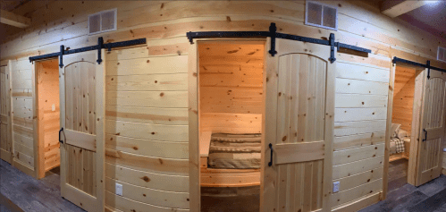 Interior view of a wooden cabin with sliding barn doors leading to cozy, small rooms. Warm, rustic decor.
