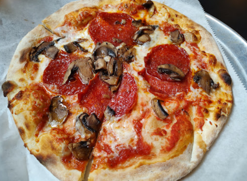 A freshly baked pizza topped with pepperoni and mushrooms, sliced and served on a white paper.