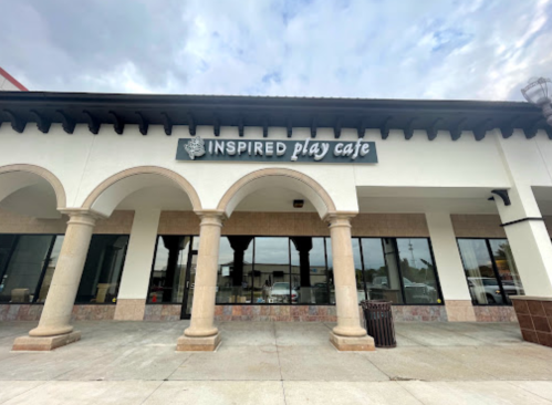 Exterior of Inspired Play Cafe, featuring arched columns and large windows under a cloudy sky.