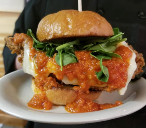 A close-up of a chicken sandwich topped with spinach and marinara sauce, served on a toasted bun.