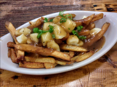 A dish of poutine featuring fries topped with cheese curds and gravy, garnished with chopped green onions.