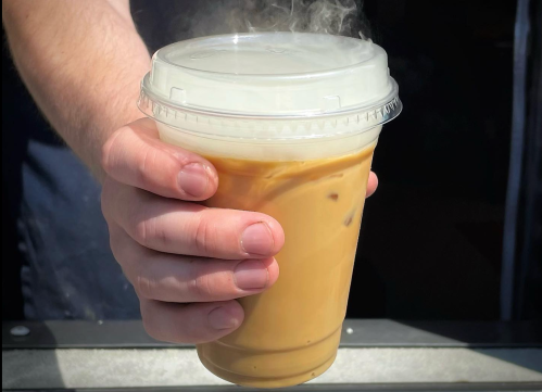 A hand holding a steaming iced coffee in a clear cup with a lid.