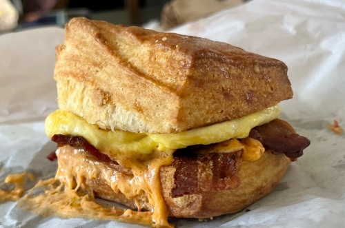 A close-up of a biscuit sandwich with bacon, egg, and melted cheese, resting on crumpled paper.
