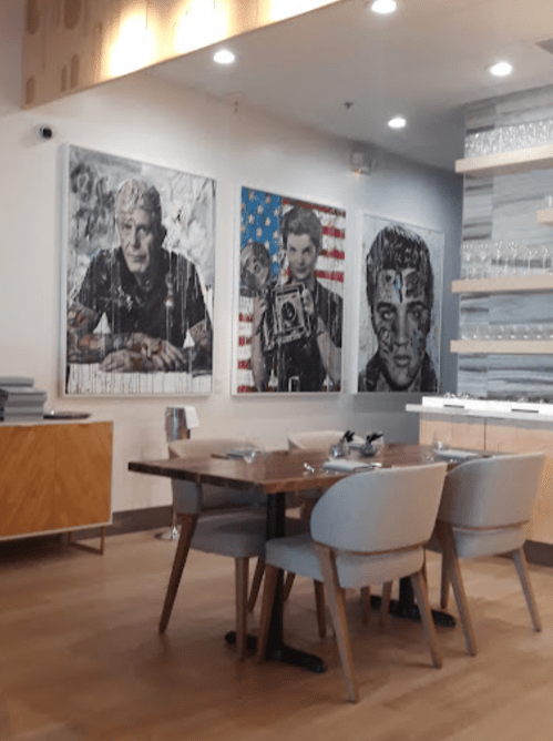 A modern dining area featuring a wooden table, chairs, and three large artistic portraits on the wall.