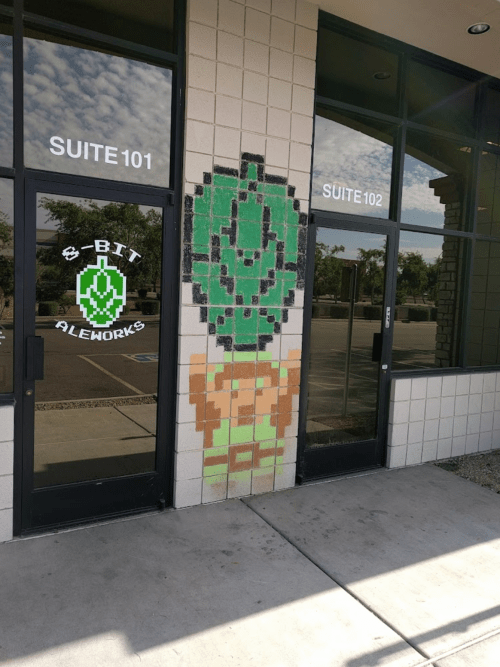 Pixel art of a green plant character on a building wall next to glass doors labeled "Suite 101" and "Suite 102."