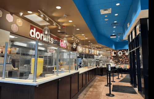 Interior of a donut shop featuring a service counter, display cases, and a coffee station, with bright blue and brown decor.