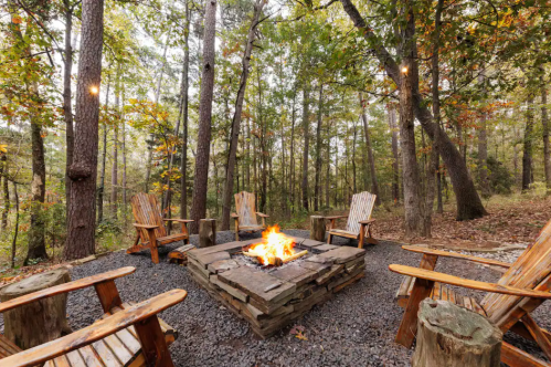 A cozy fire pit surrounded by wooden chairs in a serene forest setting with autumn foliage.