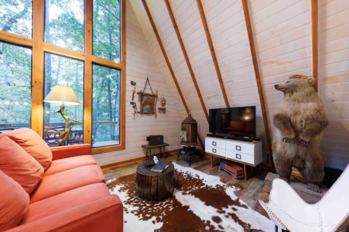 Cozy cabin interior with a bear statue, large windows, a red sofa, and rustic decor.