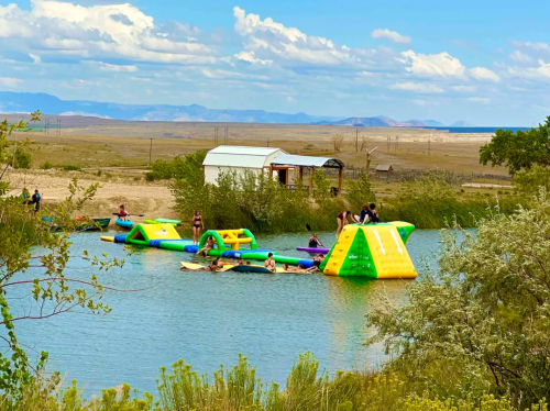 People enjoying inflatable water activities on a lake, with a backdrop of mountains and a clear blue sky.