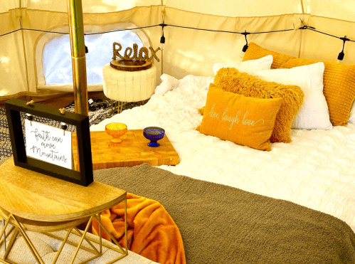 Cozy tent interior with a bed, decorative pillows, a wooden table, and warm lighting, creating a relaxing atmosphere.