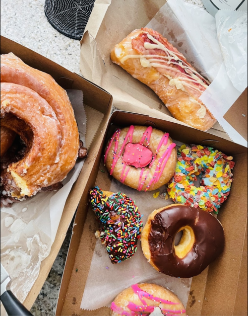 A variety of colorful donuts and pastries in a box, including a glazed croissant, sprinkled donuts, and a cream-filled pastry.