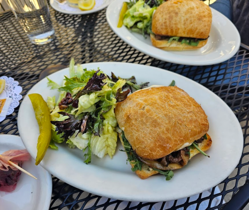 A sandwich on a plate with a side salad and pickles, served on a black metal table.