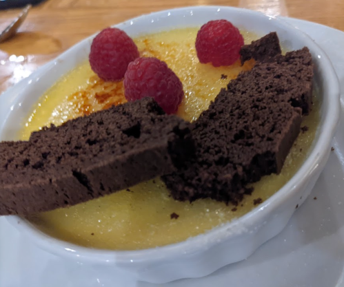 A creamy dessert topped with raspberries and chocolate biscotti in a white dish.