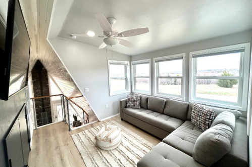 Cozy living area with a gray sofa, large windows, and a ceiling fan, featuring a modern design and scenic view.