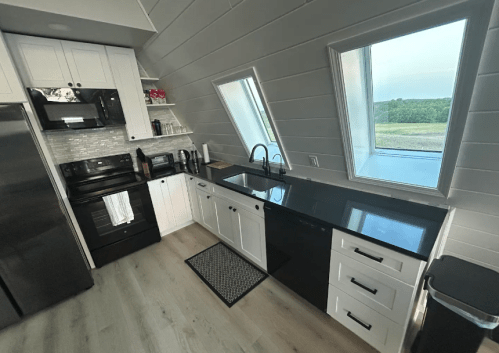 Modern kitchen with black and white cabinetry, stainless steel appliances, and large windows overlooking greenery.