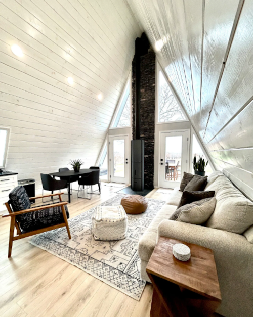 Cozy A-frame living room with a sofa, armchair, dining area, and large windows overlooking a patio.