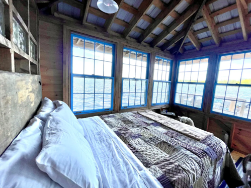 Cozy bedroom with a quilted bedspread and large windows overlooking a serene body of water.