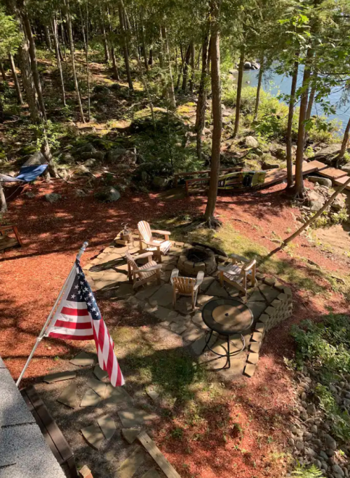 A serene outdoor space with chairs, a table, and an American flag, surrounded by trees and a rocky landscape.