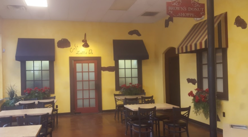 Cozy café interior with yellow walls, window decorations, and tables, featuring a sign for Brown's Donut Shoppe.