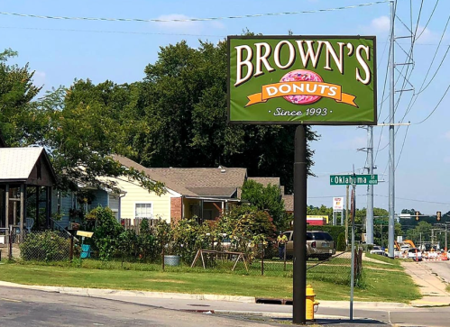 Sign for Brown's Donuts, established in 1993, with a residential area and street sign visible in the background.