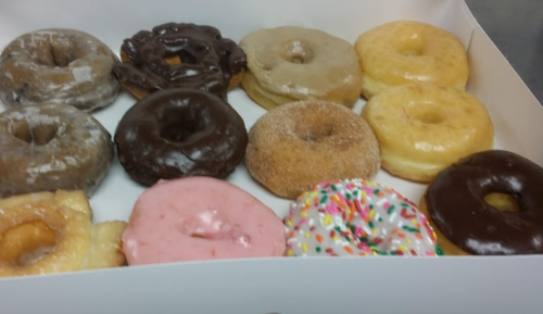 A box of assorted donuts, including glazed, chocolate, pink frosted, and sprinkled varieties.