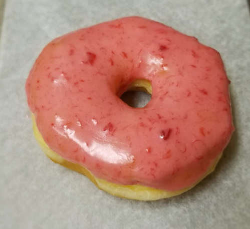 A round donut with a glossy pink strawberry glaze on a light background.