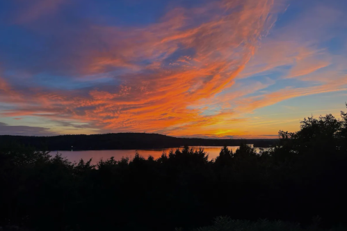 A vibrant sunset over a calm lake, with colorful clouds and silhouettes of trees in the foreground.