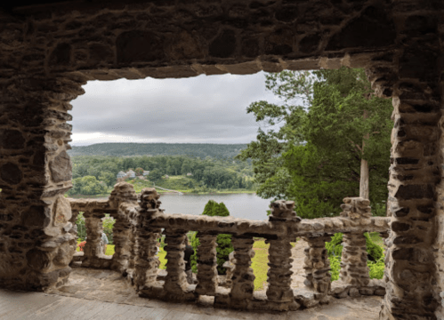 View from a stone archway overlooking a serene lake and lush greenery under a cloudy sky.
