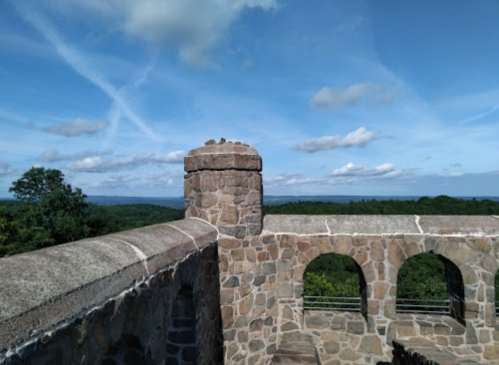View from a stone tower overlooking a lush green landscape and blue sky with scattered clouds.