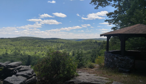 A scenic view of lush green hills under a blue sky with clouds, featuring a gazebo in the foreground.