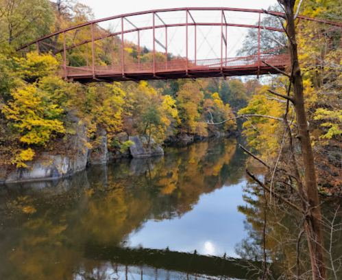 A red bridge spans a calm river, surrounded by vibrant autumn foliage and rocky banks.