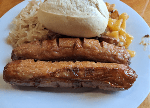 A plate with two grilled sausages, a roll, sauerkraut, and cheesy potatoes.