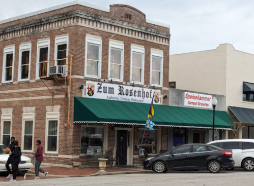 Exterior of Zum Rosenhof, an authentic German restaurant, with a green awning and nearby German grocery store.