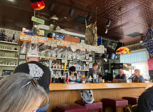 A cozy bar scene with patrons at the counter, shelves of drinks, and a warm, inviting atmosphere.
